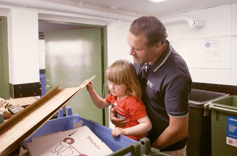 En vuxen och ett barn sorterar sopor i ett miljörum
