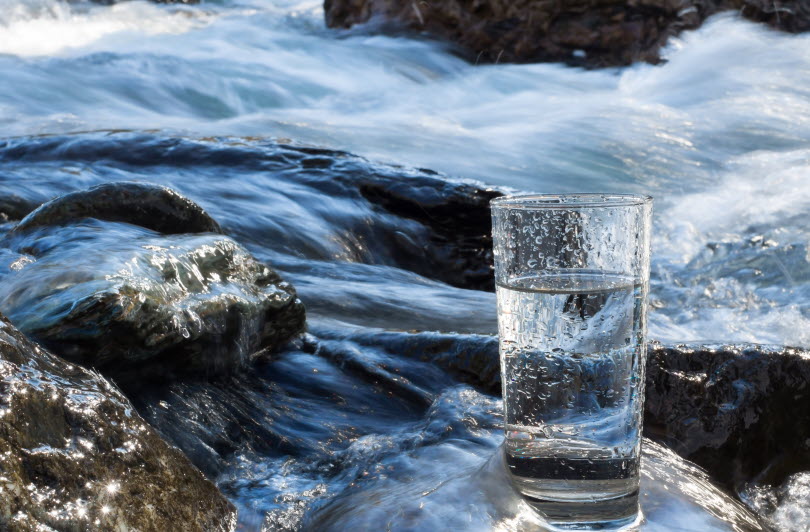Ett glas med vatten som står på stenar vid ett vattendrag